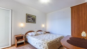 A bedroom with a bed, bedside tables, a nightstand, a wall-mounted light, a framed picture, and a wooden wardrobe.