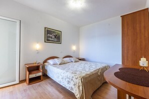 A bedroom with a bed, bedside tables, a nightstand, a wall-mounted light, a framed picture, and a wooden wardrobe.