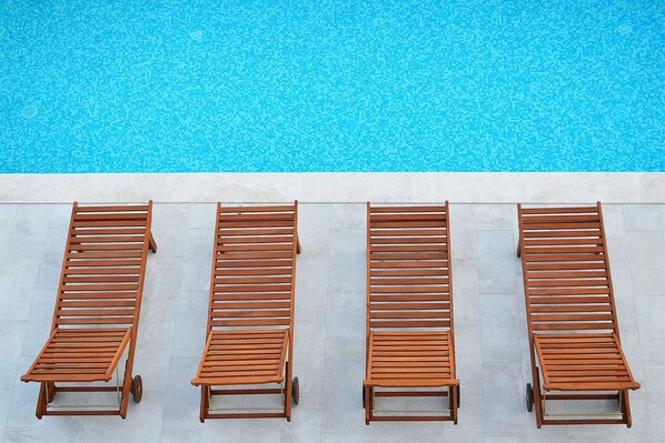 A row of wooden lounge chairs aligned parallel to a swimming pool.