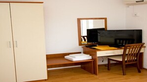 A room with a wooden desk, a chair, a television, and a wardrobe.