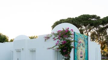 Un edificio blanco con un mural lateral, rodeado de vegetación y árboles.