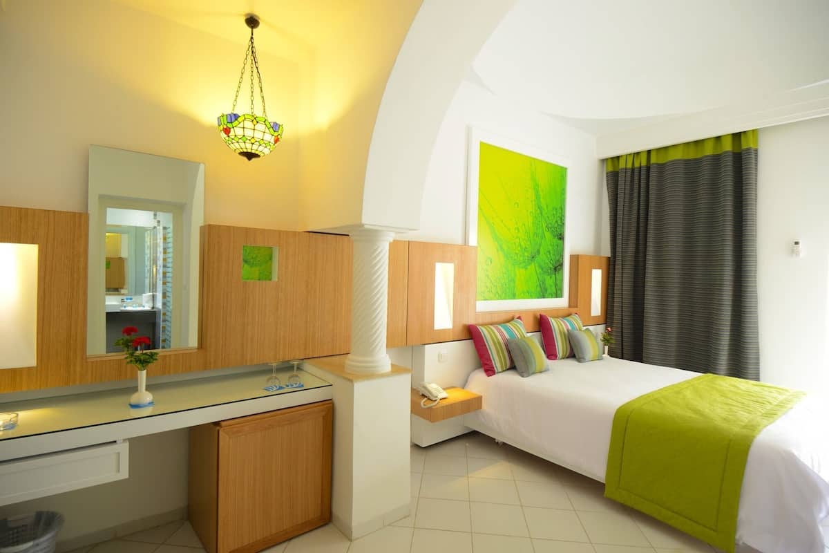 Ein modernes Hotelzimmer mit Bett, Nachttisch, Lampe und einem großen Spiegel.