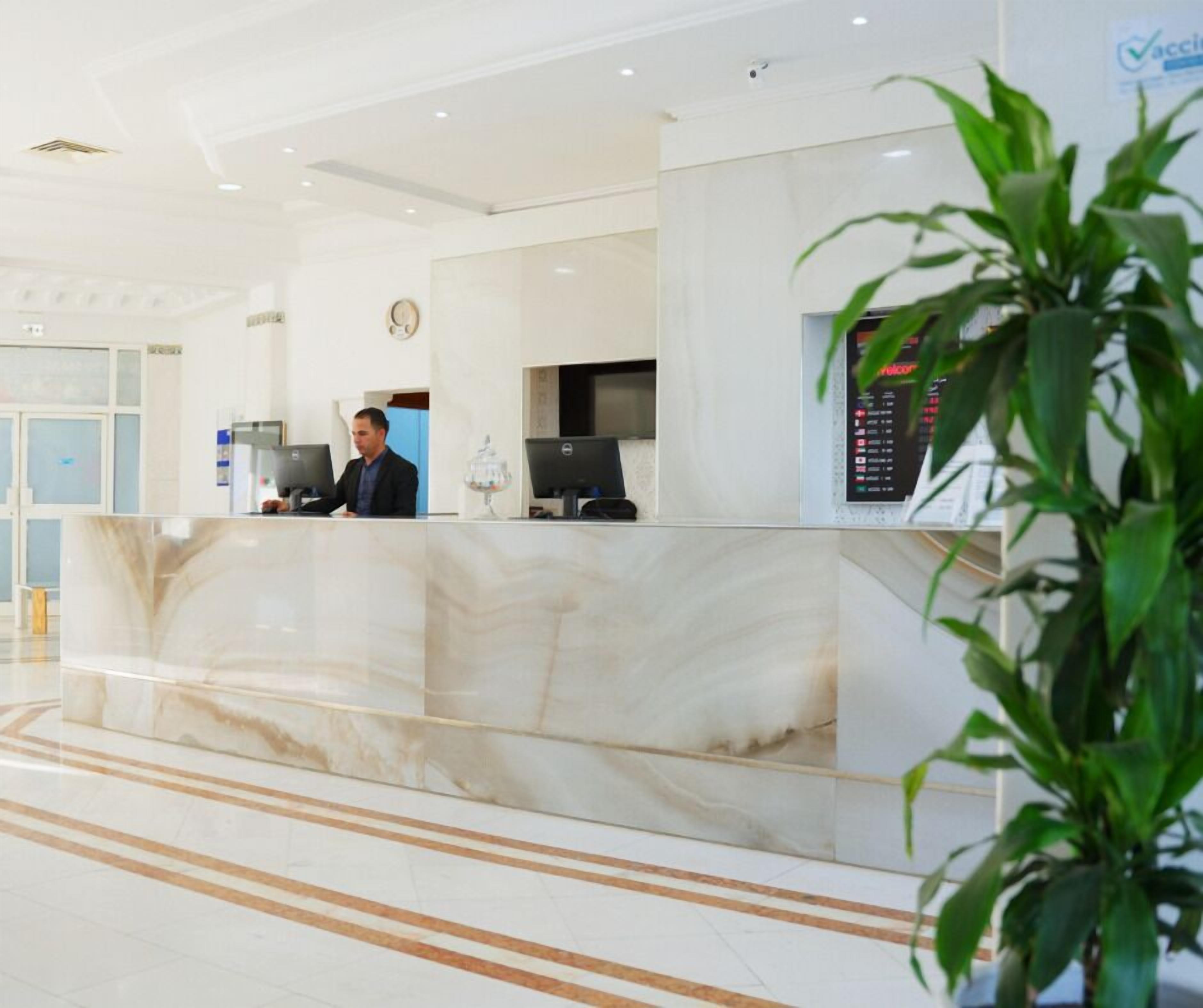 A hotel reception area with a marble counter, a digital display, and a clock on the wall.