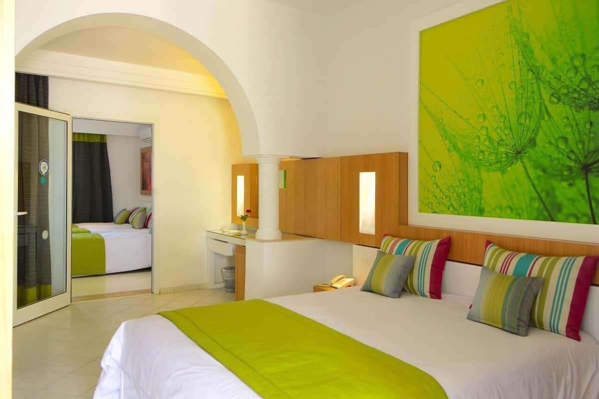 Ein modernes Hotelzimmer mit einem großen Bett, einem Schreibtisch, einem Spiegel und einem abstrakten grünen Gemälde an der Wand.