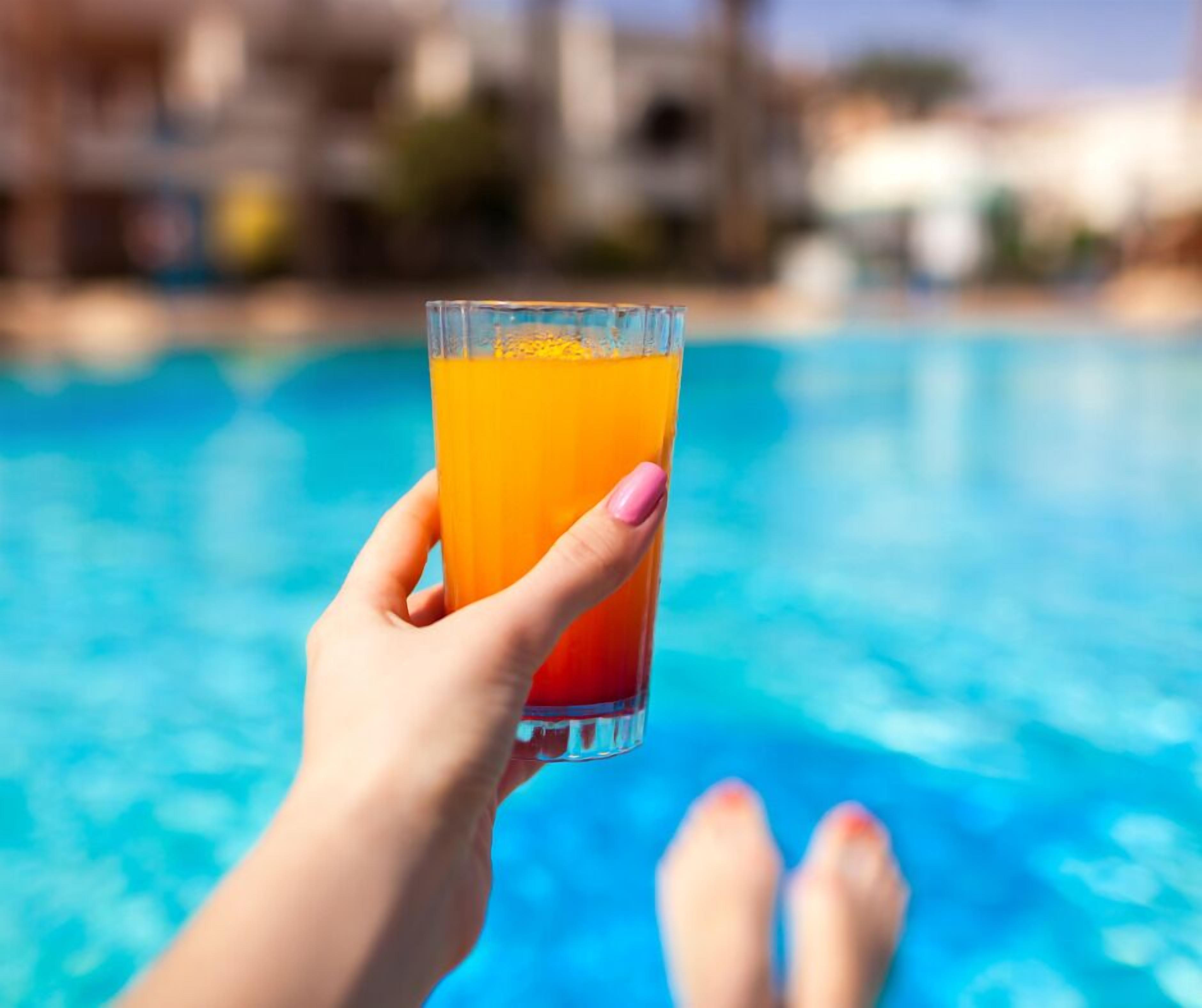 Una mano che tiene un bicchiere di succo d'arancia sopra una piscina.