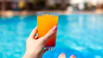 Una mano che tiene un bicchiere di succo d'arancia sopra una piscina.