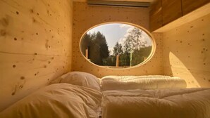Une pièce dotée d’une fenêtre ronde, de murs en bois et d’un lit recouvert de draps blancs.