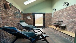 A spa area with brick walls, two massage chairs, a small shelf with a bowl and a container, and a door leading outside. - Charming Stay in Sveti Križ (Tuhelj)