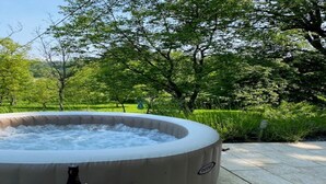 A hot tub in an outdoor setting with a table and bottle in front. - Charming Stay in Sveti Križ (Tuhelj)