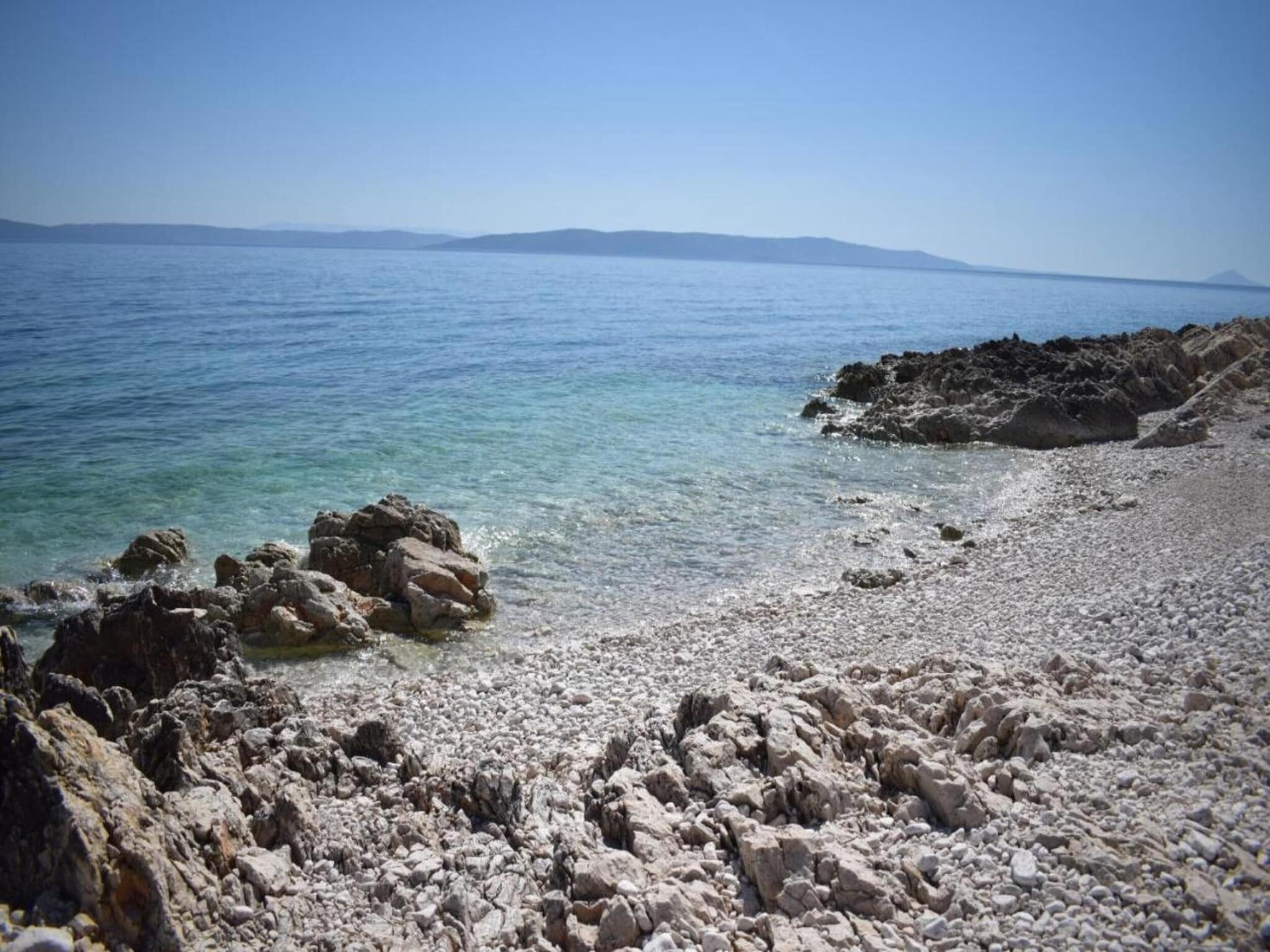 Un littoral rocheux, avec une eau claire et des montagnes qui se dessinent à l’horizon.