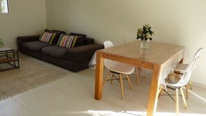 A living room with a brown sofa, a wooden dining table, and white chairs. - Mini villa in the heart of a pretty garden (Porto-Vecchio)
