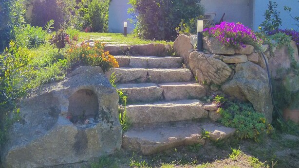 A stone staircase leading to a building with a tiled roof, surrounded by lush greenery and flowering plants. - Mini villa in the heart of a pretty garden (Porto-Vecchio)