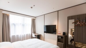 Een hotelkamer met een bed, een bureau, een televisie, een spiegel en een kapstok.