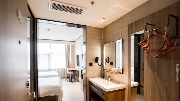 Een moderne hotelkamer met een bed, een bureau, een badkamer met spiegel en een kapstok.