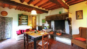Una sala de estar acogedora con chimenea, vigas de madera, una mesa de comedor con sillas y un sofá con cojines.