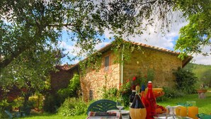 Un área de comedor al aire libre con una mesa dispuesta para dos personas, rodeada de follaje y un edificio de piedra.