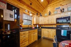 Una cocina tipo cabaña de madera con refrigerador, estufa, microondas y gabinetes de madera.