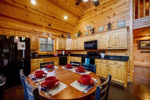 Interior de una cabaña de madera con una mesa de comedor preparada para cuatro personas, armarios de cocina, un refrigerador y un microondas.