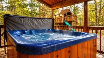 A hot tub on a wooden deck with a wooden playhouse in the background.