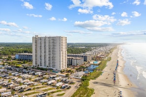 A high-rise hotel with multiple floors, a beachside location, and a parking area with RVs.