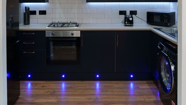 Una cocina moderna con gabinetes negros, una campana extractora de acero inoxidable, un microondas y una lavadora debajo de un arco.