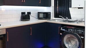 Una cocina compacta con armarios oscuros, un microondas, un tostador y una lavadora.
