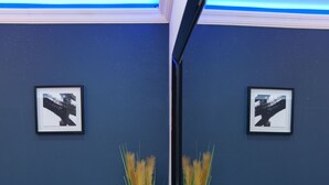 Una habitación con una pared azul, dos cuadros enmarcados, un otoman tapizado, una mesita y una planta.