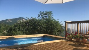 Una terraza de madera con piscina, plantas en macetas y vistas a la montaña.