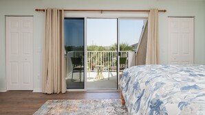 Un dormitorio con cama, ventilador de techo, puerta corrediza de vidrio a un balcón y vistas al exterior.