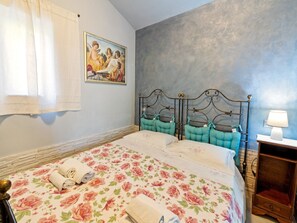 A bedroom with a floral bedspread, a metal headboard, a painting on the wall, and a bedside table with a lamp.