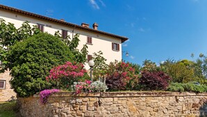 A stone wall with a building behind it, featuring a window and a lamp post. - Countryside Home in Arezzo with Pool (Tregozzano, Arezzo)