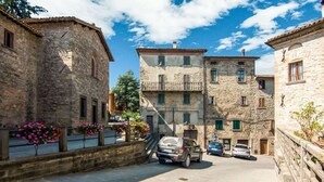 A narrow street with stone buildings, parked cars, and flower boxes. - Panoramic Countryside Home (Apecchio)
