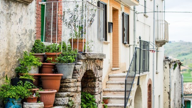Una calle estrecha con una escalera de piedra que lleva a un edificio con varios balcones, cada uno decorado con macetas de plantas.