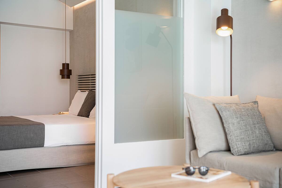 A modern bedroom with a bed, a bedside table with glasses, and a wall-mounted lamp.
