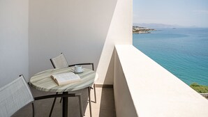 A small balcony with a round table, two chairs, and a book. The balcony overlooks a body of water and distant land. - Kakkos Bay (Ierapetra)