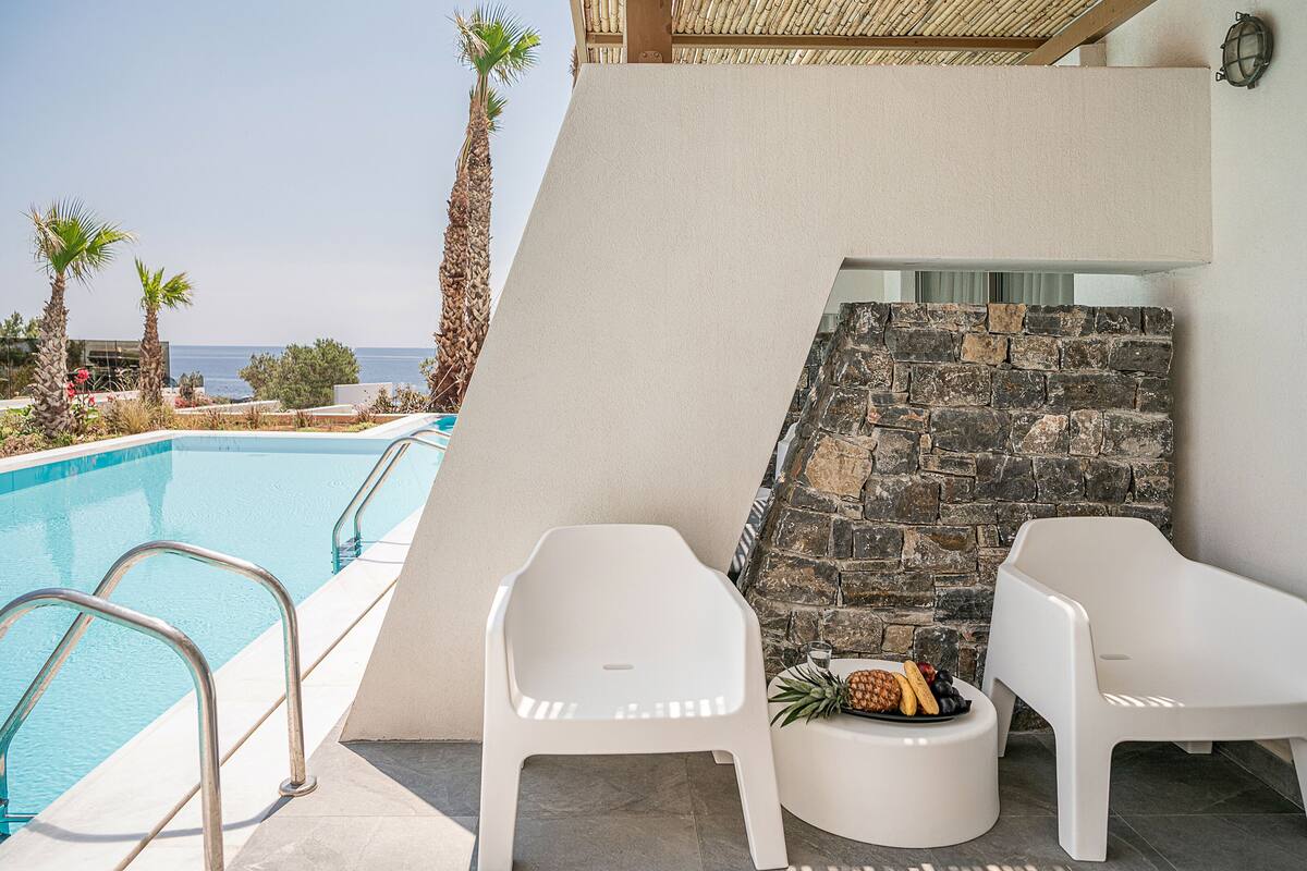 A poolside area with a stone wall, two white plastic chairs, and a fruit bowl.