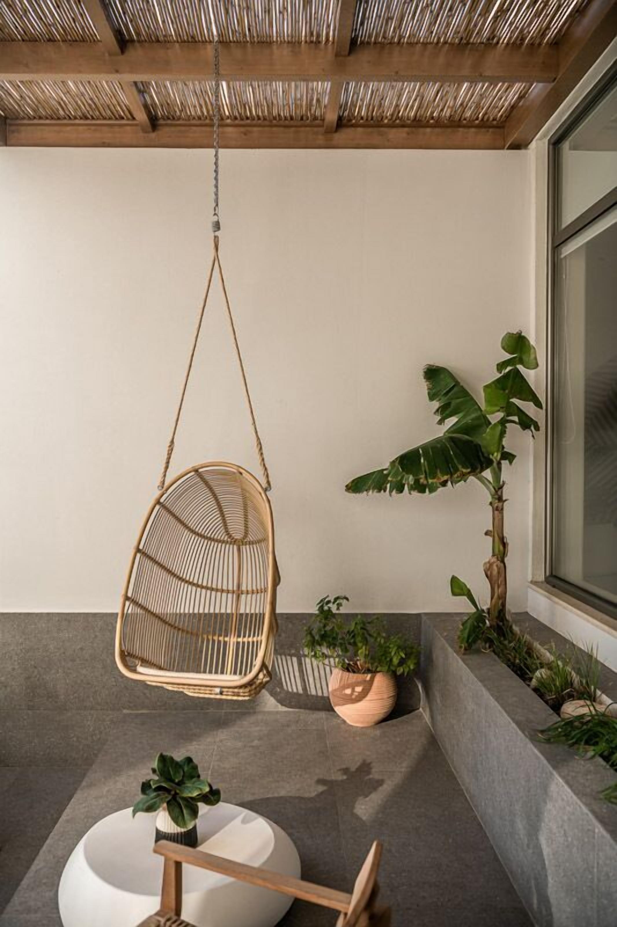 A hanging chair, a potted plant, and a round table in a modern interior space.