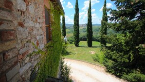 A rustic stone building with ivy-covered walls, a gravel path leading to a grassy area with tall cypress trees, and a clear blue sky. - Elysian Escape - A paradise (San Venanzo)