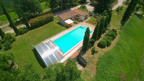 A large swimming pool with a glass-enclosed hot tub, surrounded by lush greenery and a small house. - Elysian Escape - A paradise (San Venanzo)