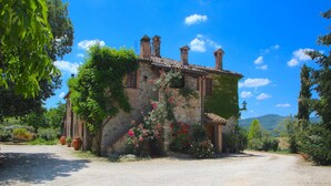 A rustic stone building with a gravel driveway, surrounded by lush greenery and flowering plants. - Elysian Escape - A paradise (San Venanzo)