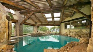 Ein Innenpool mit Steinwänden, Holzbalkendecke und großen Fenstern.