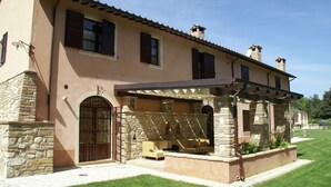 Una casa de dos plantas con fachada de piedra, un porche cubierto con mobiliario exterior y un césped bien cuidado.