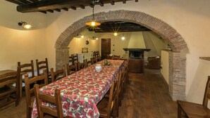 Un comedor con una larga mesa cubierta por un mantel floral, sillas de madera y un arco de ladrillo.
