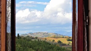 Vista a través de una ventana que muestra un paisaje con un pueblo en una colina, árboles y cielo despejado.