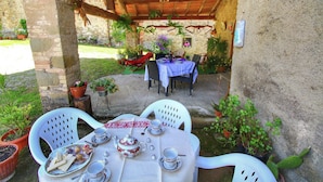 Un patio al aire libre con una mesa preparada para tomar té, rodeado de plantas en macetas y un rústico muro de piedra.