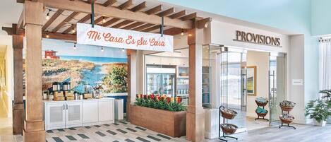 A hotel lobby with a wooden pergola, a mural of a coastal scene, and a sign that reads "Mi Casa Es Su Casa".