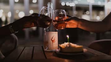 Dos manos chocando copas de vino junto a una botella de vino Dacinio y una vela sobre una mesa.