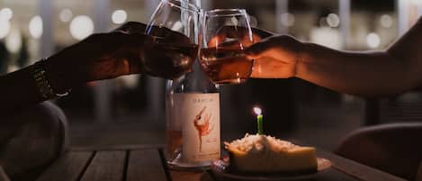 Dos manos chocando copas de vino junto a una botella de vino Dacinio y una vela sobre una mesa.