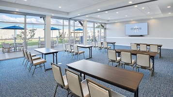 A conference room with tables and chairs, large windows, and a screen displaying the Compass brand.
