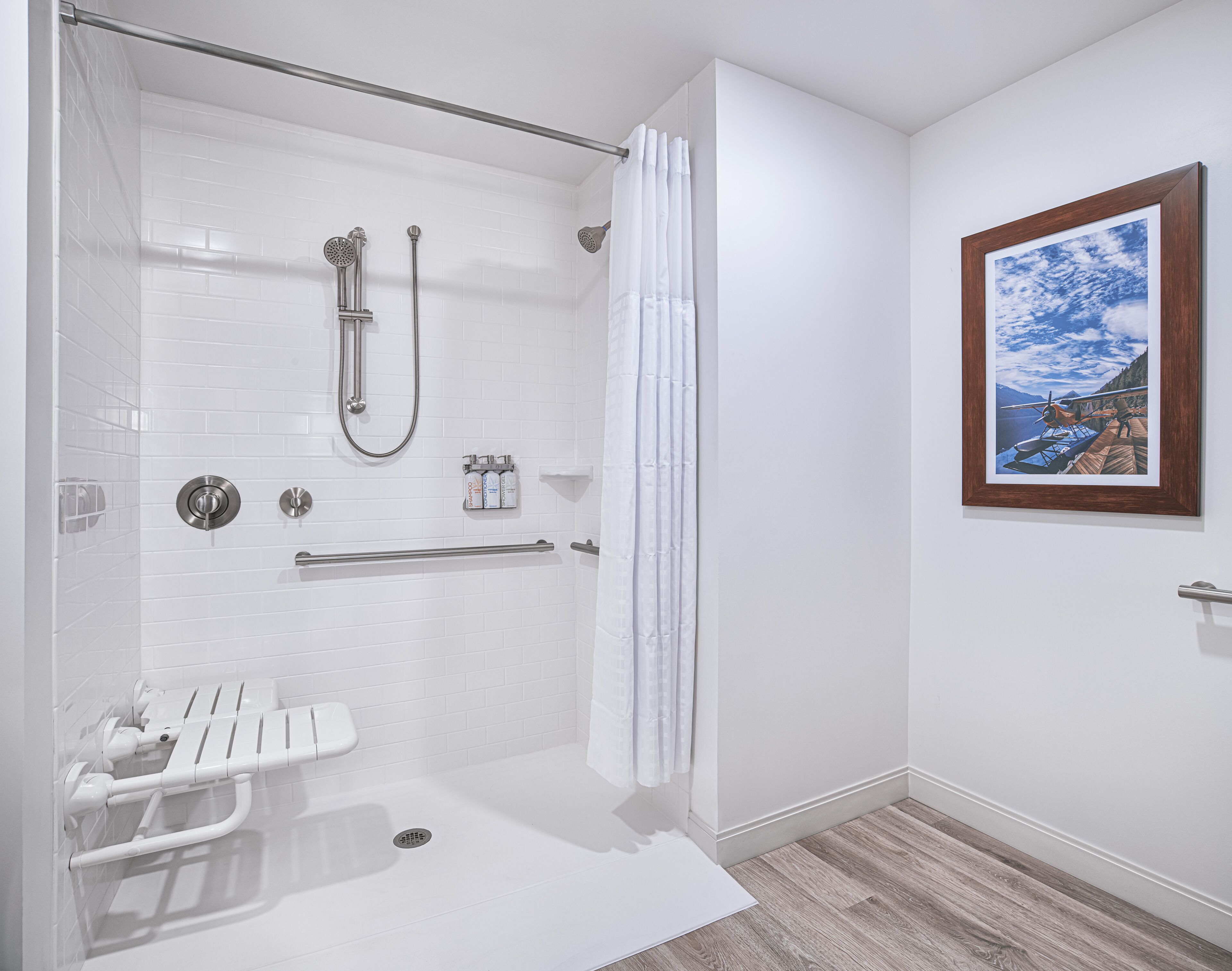 A modern bathroom with a walk-in shower, a toilet with grab bars, and a wooden floor.